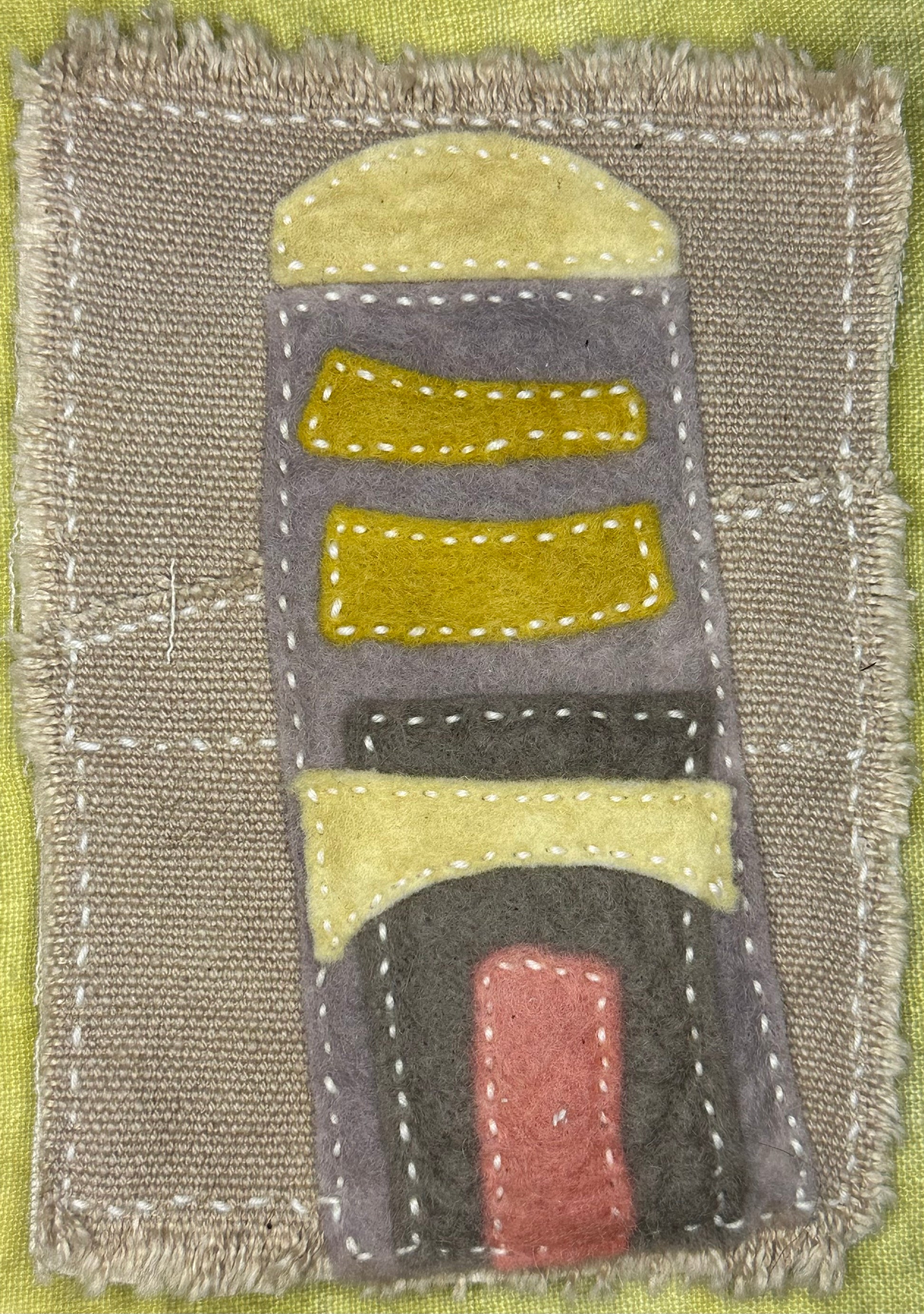 Fragments of Home textile art by Suzanne Gibbs with layered felt shapes in yellow, gray, black, and pink, hand-stitched with white thread resembling a tower.