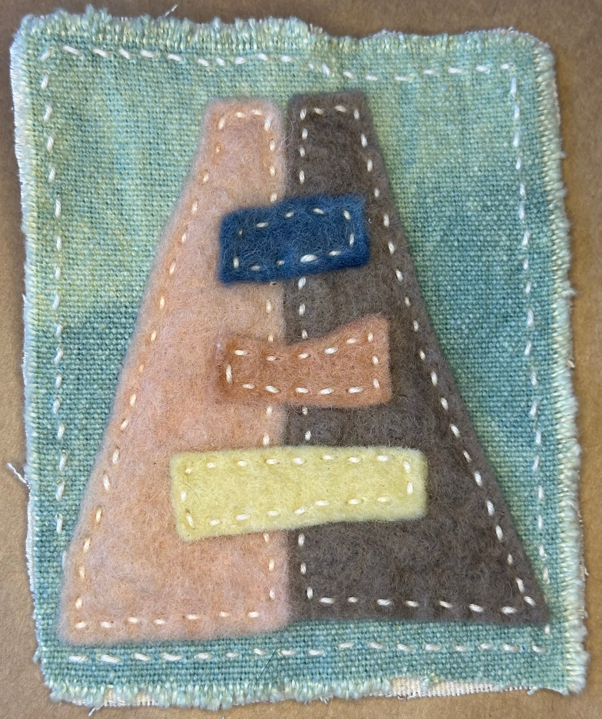 A stylized A-Frame textile artwork by Suzanne Gibbs from her Fragments of Home series made of different colored felt pieces on a hand-died hemp fabric background.