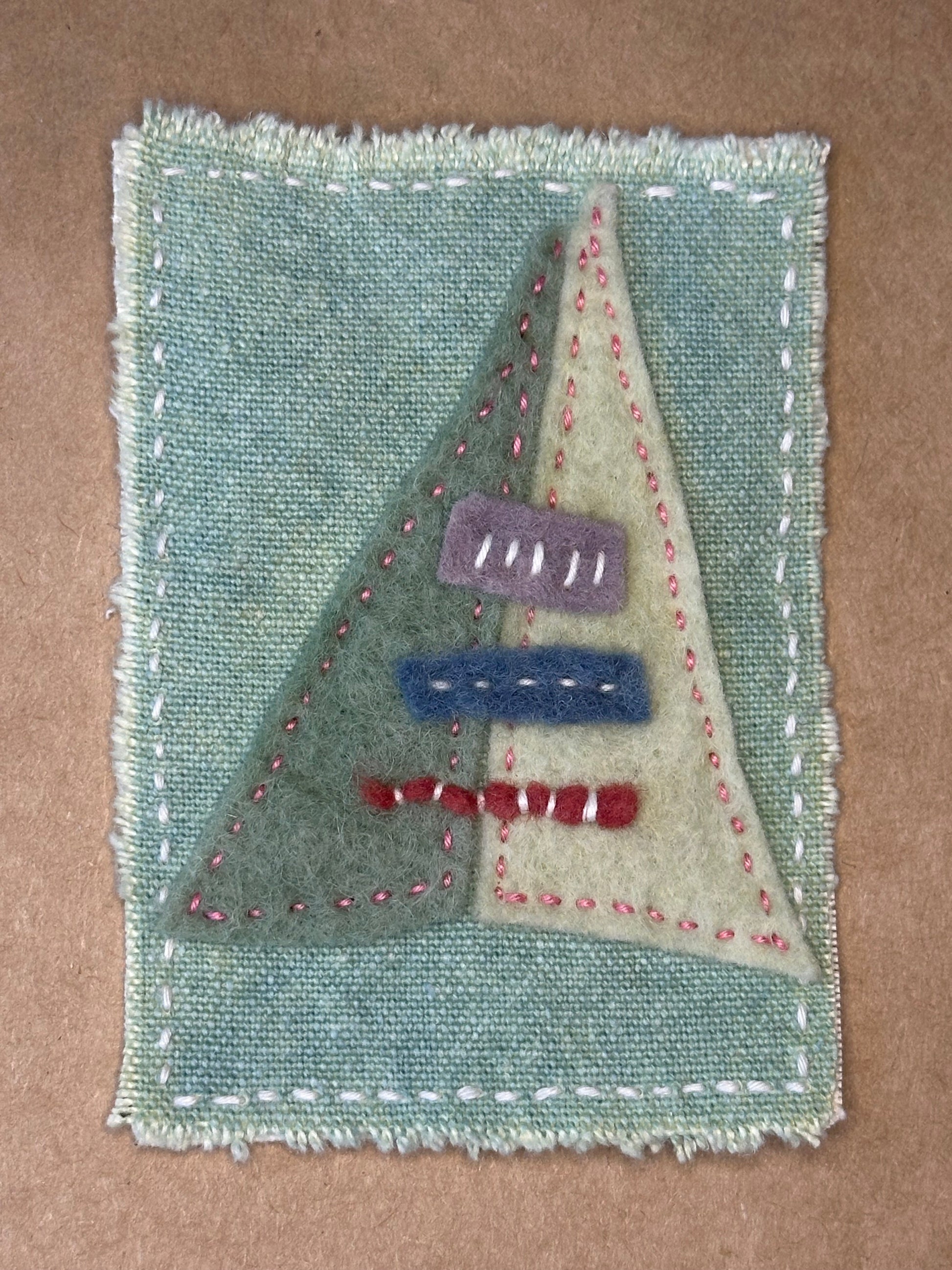 A small artwork by Suzanne Gibbs depicting a teepee made with cotton, felt, and thread on a pale green background.