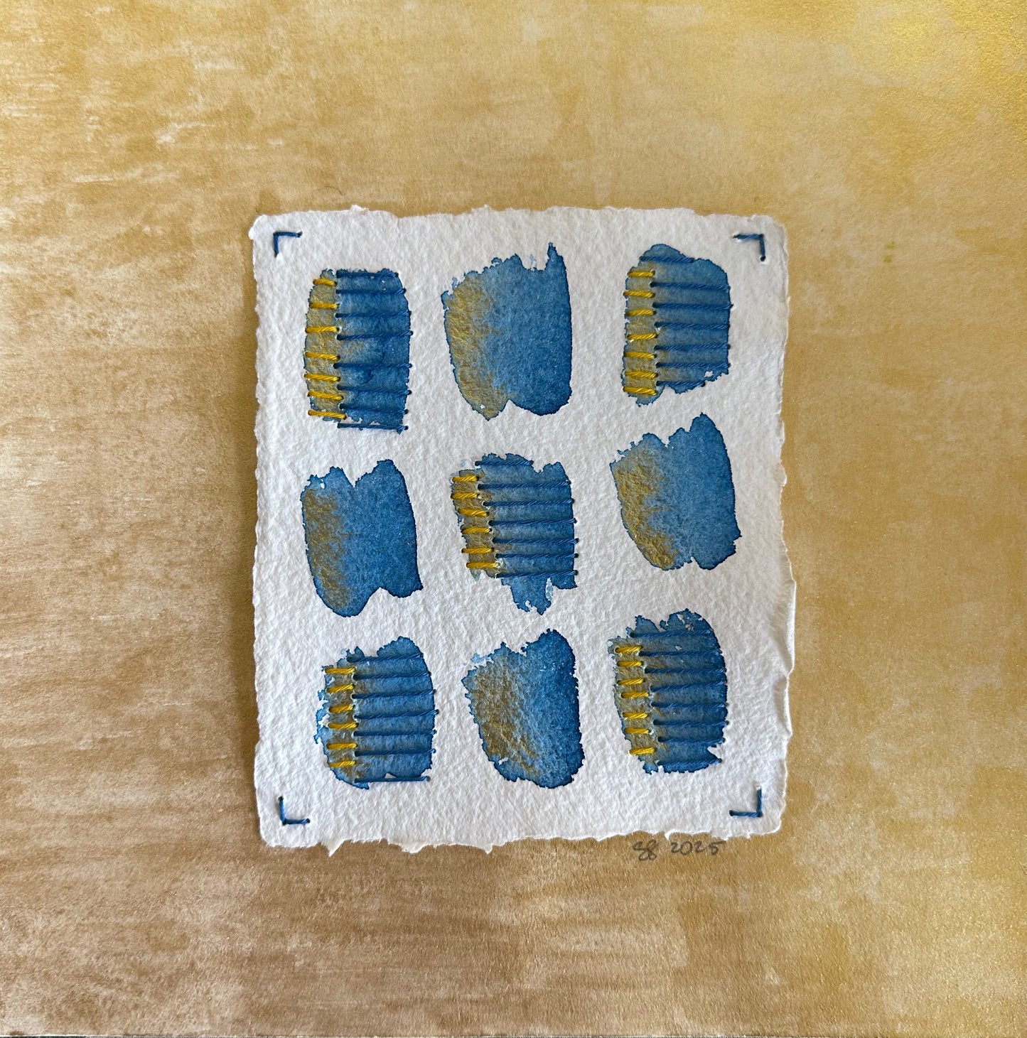 A collage painting by Suzane Gibbs featuring a series of stitched, geometrically shaped areas on watercolor paper with a gold background.