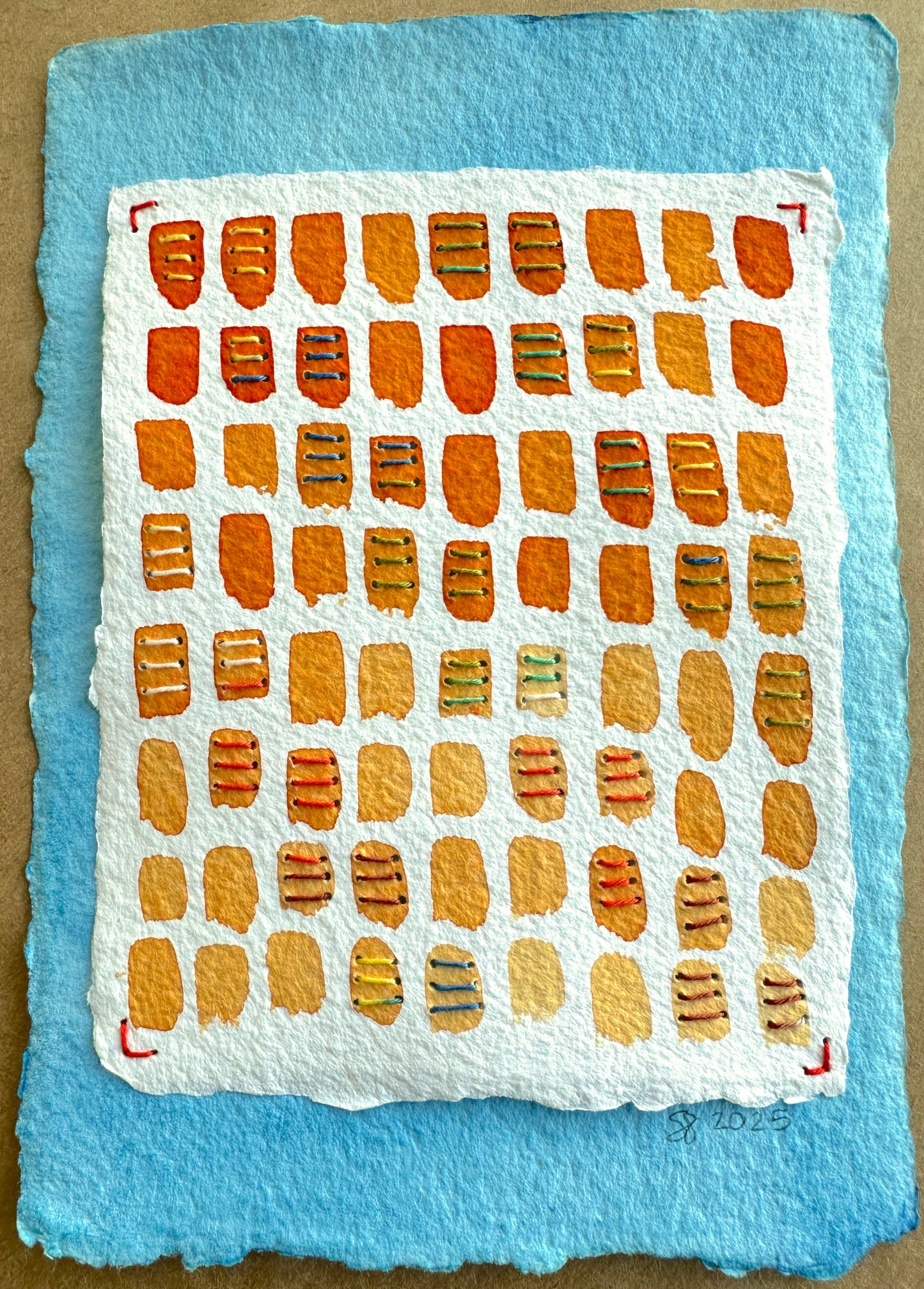 A handcrafted collage painting by Suzanne Gibbs featuring a grid of orange and yellow stitched rectangles on a blue watercolor background.