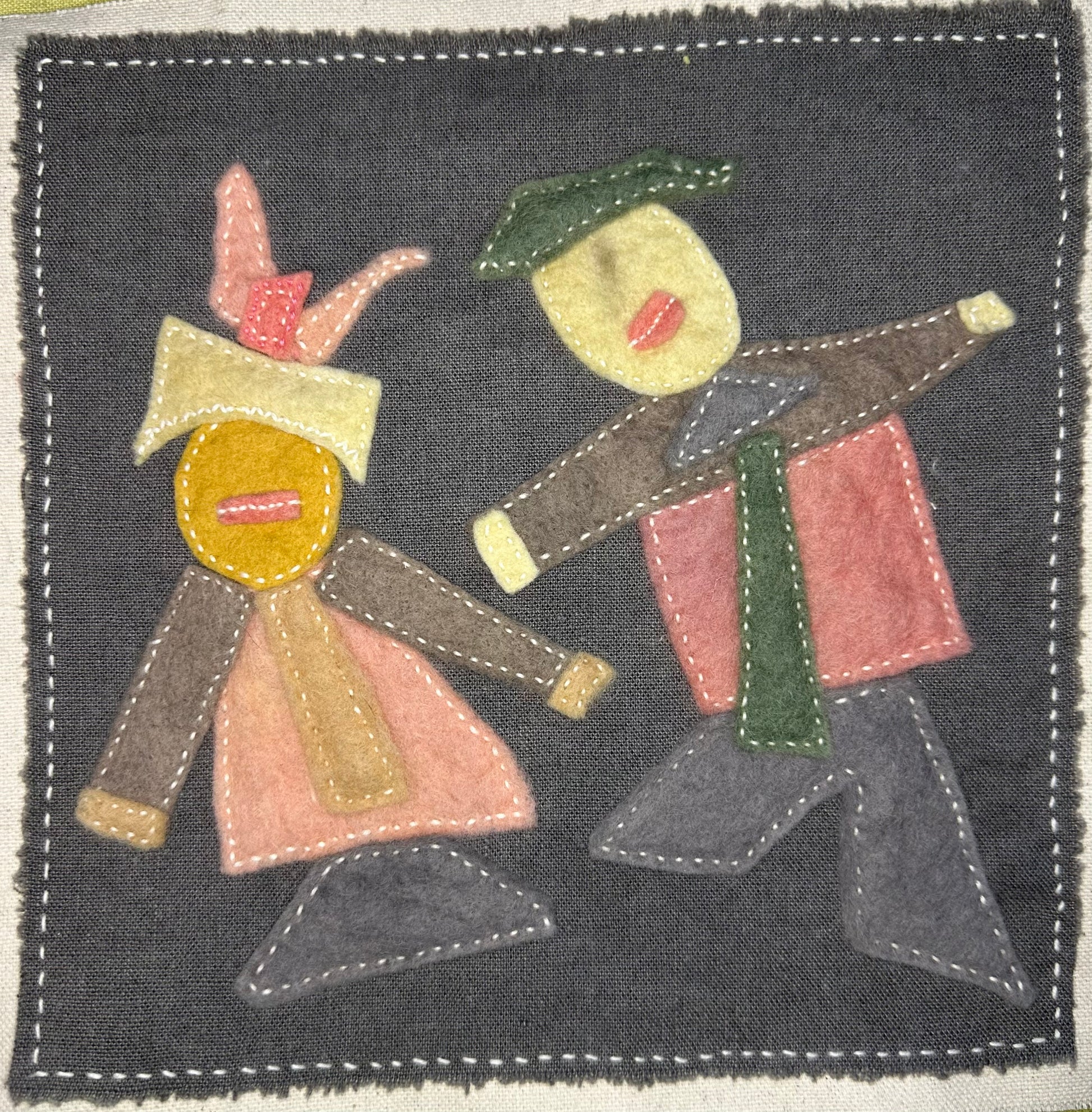 Fragments of Home textile art by Suzanne Gibbs with two abstract felt figures in pink, brown, green, and yellow on a dark gray fabric background, hand-stitched in white.