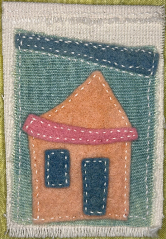 Fragments of Home textile art by Suzanne Gibbs with a peach-colored felt house, pink roof, and blue windows on a teal background, hand-stitched in white.