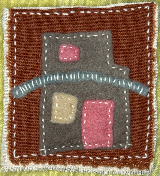 Fragments of Home textile art by Suzanne Gibbs with a gray felt house form, pink and beige windows, and a curved blue line on a brown background, hand-stitched in white.