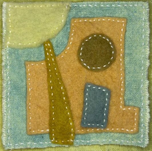 Fragments of Home textile art by Suzanne Gibbs with a tan felt house, green abstract tree, brown circle window, and blue rectangle on a pale blue fabric background, hand-stitched in white.