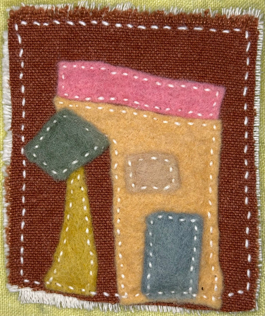 Fragments of Home textile art by Suzanne Gibbs with a peach felt house, pink roof, blue door, tan window, and an angled green-and-yellow abstract tree on a brown fabric background, hand-stitched in white.
