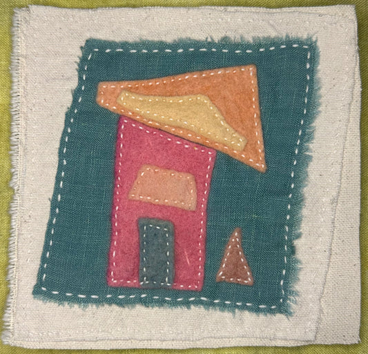 Fragments of Home textile art by Suzanne Gibbs with a pink felt house, orange and yellow slanted roof, green door, and small brown triangle beside it on a teal fabric background, hand-stitched in white.