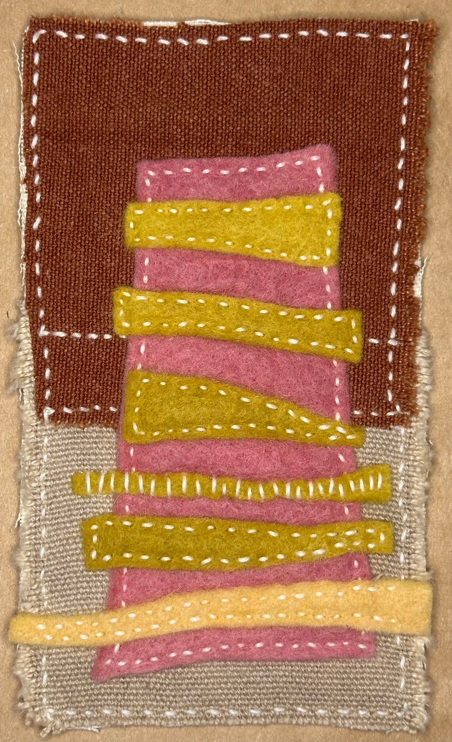 Fragments of Home textile art by Suzanne Gibbs with a pink felt apartment building accented by yellow stitched bands on brown and tan fabric, hand-stitched in white.