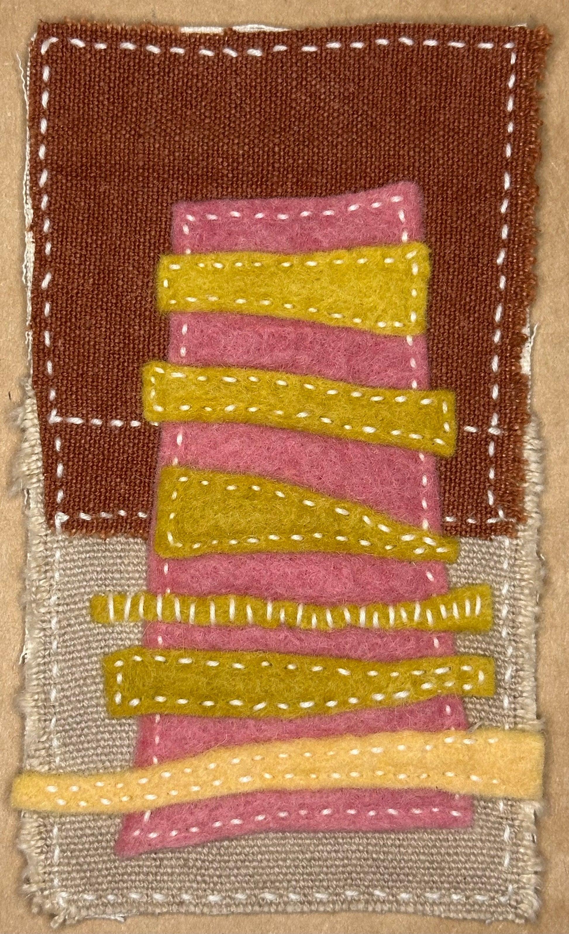 Fragments of Home textile art by Suzanne Gibbs with a pink felt apartment building accented by yellow stitched bands on brown and tan fabric, hand-stitched in white.