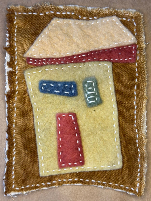 Textile artwork by Suzanne Gibbs from her Fragments of Home series, created with felt and Sashiko stitching, featuring a stylized house shape in warm gold, red, and cream tones.