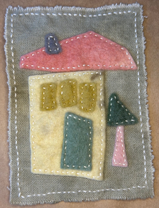Fabric house with a pink roof, yellow windows, and a green door on a warm gray background by Suzanne Gibbs.