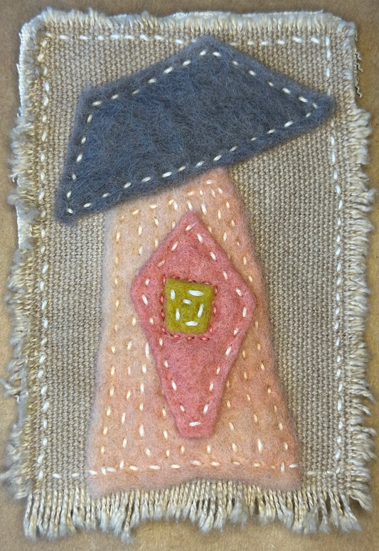 Textile art piece by Suzanne Gibbs with pink and blue shapes resembling a home on a beige background